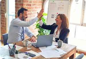 Happy business colleagues high-fiving at a desk with a laptop and documents, celebrating successful Reg A Filings.
